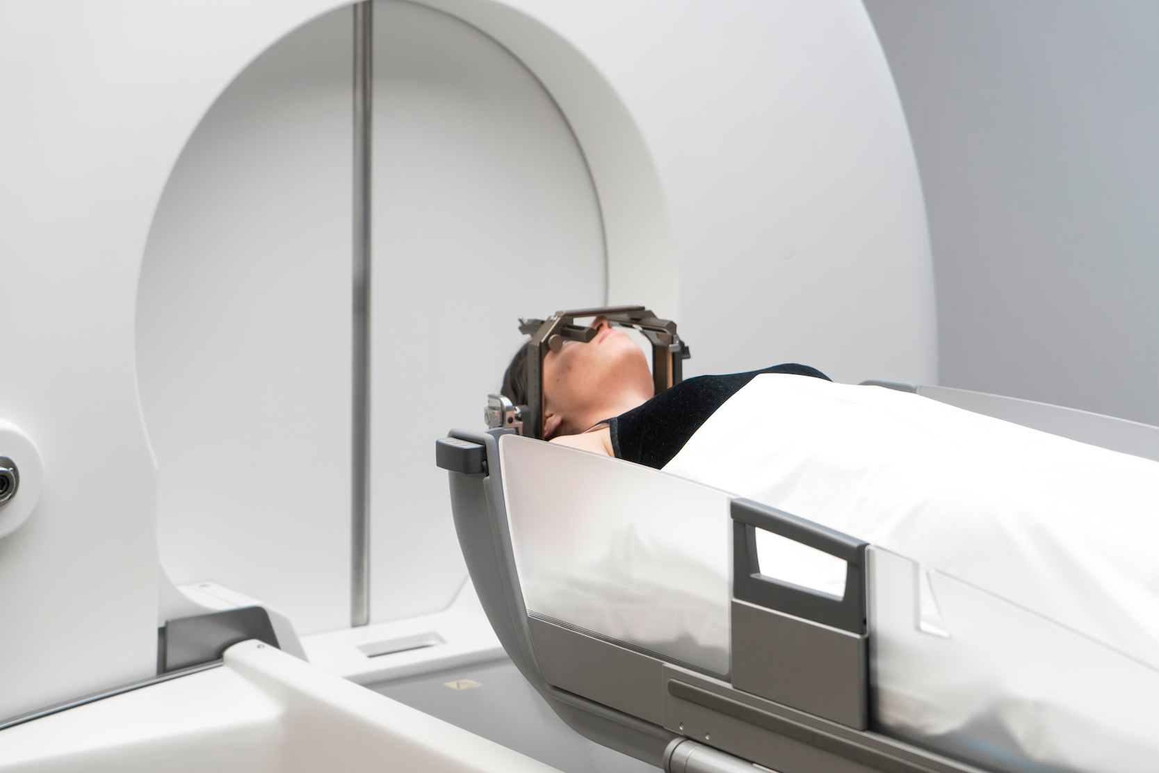 The patient lies in front of the device for the treatment of cancer with a gamma knife. She has a metal clip cap on his head.