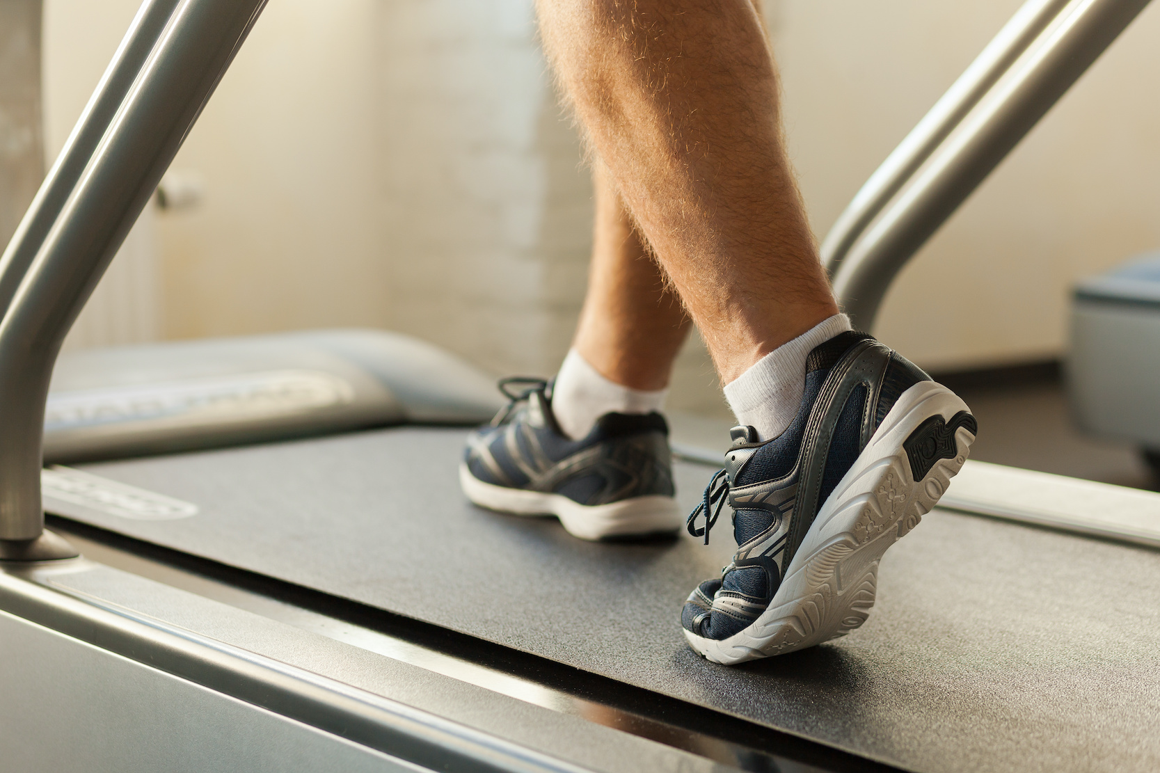 Exercising on treadmill. Close-up of man walking by treadmill in sports club
