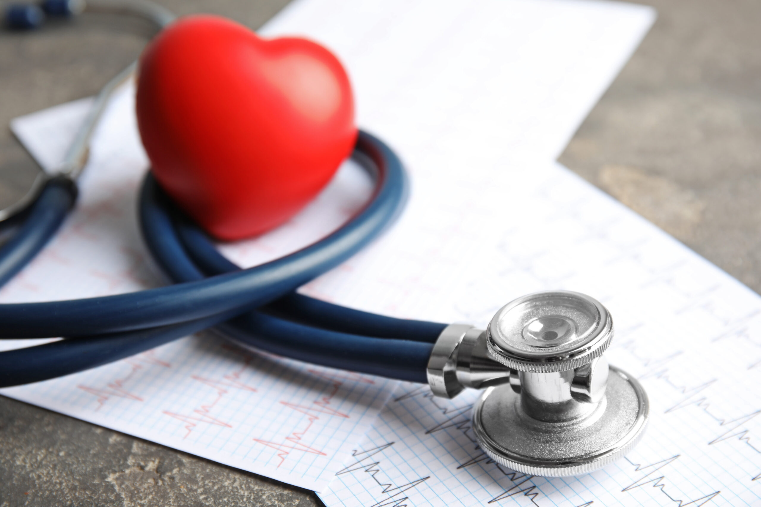 Stethoscope, red heart and cardiogram on gray table. Cardiology
