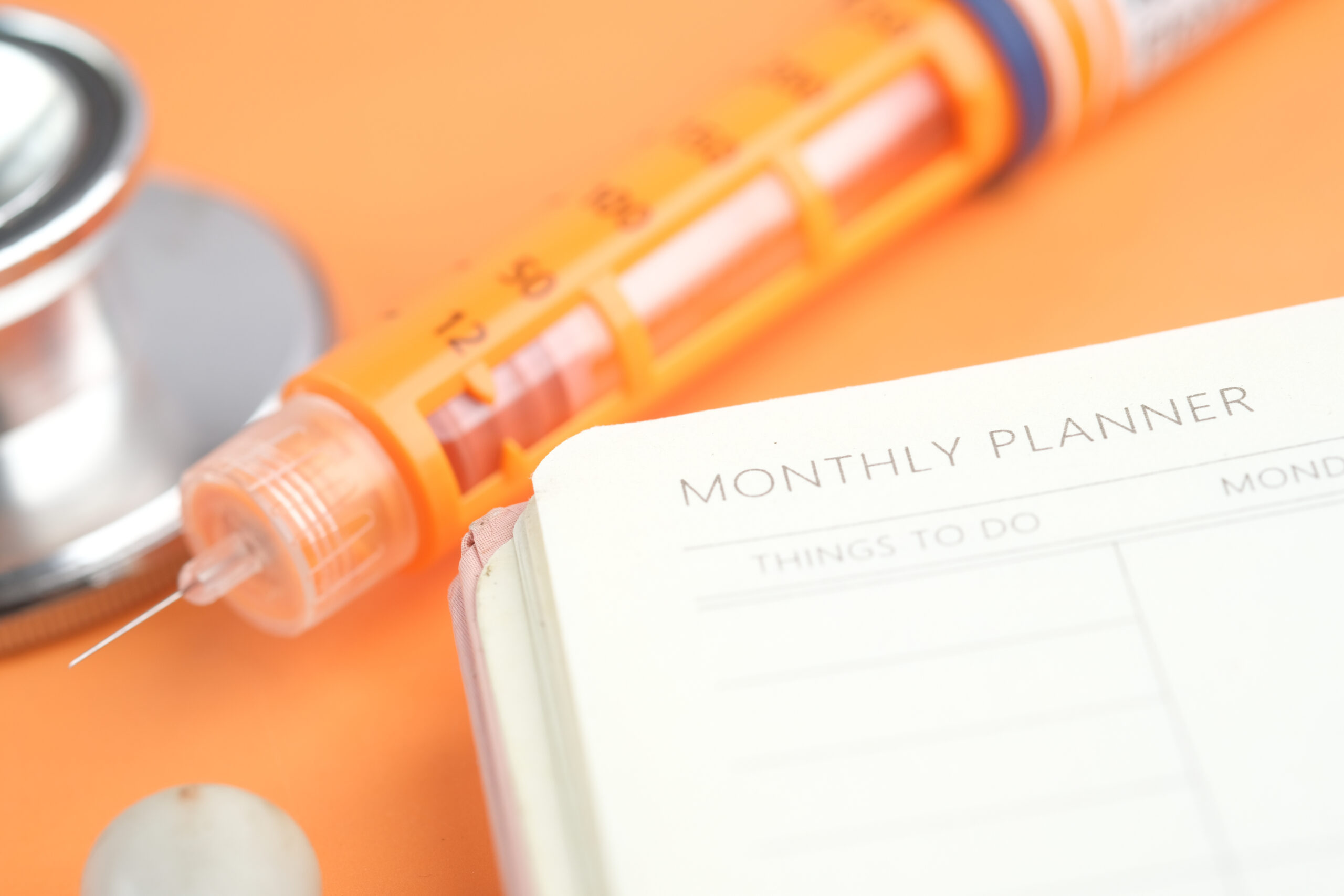 Insulin pen and weekly planner on table