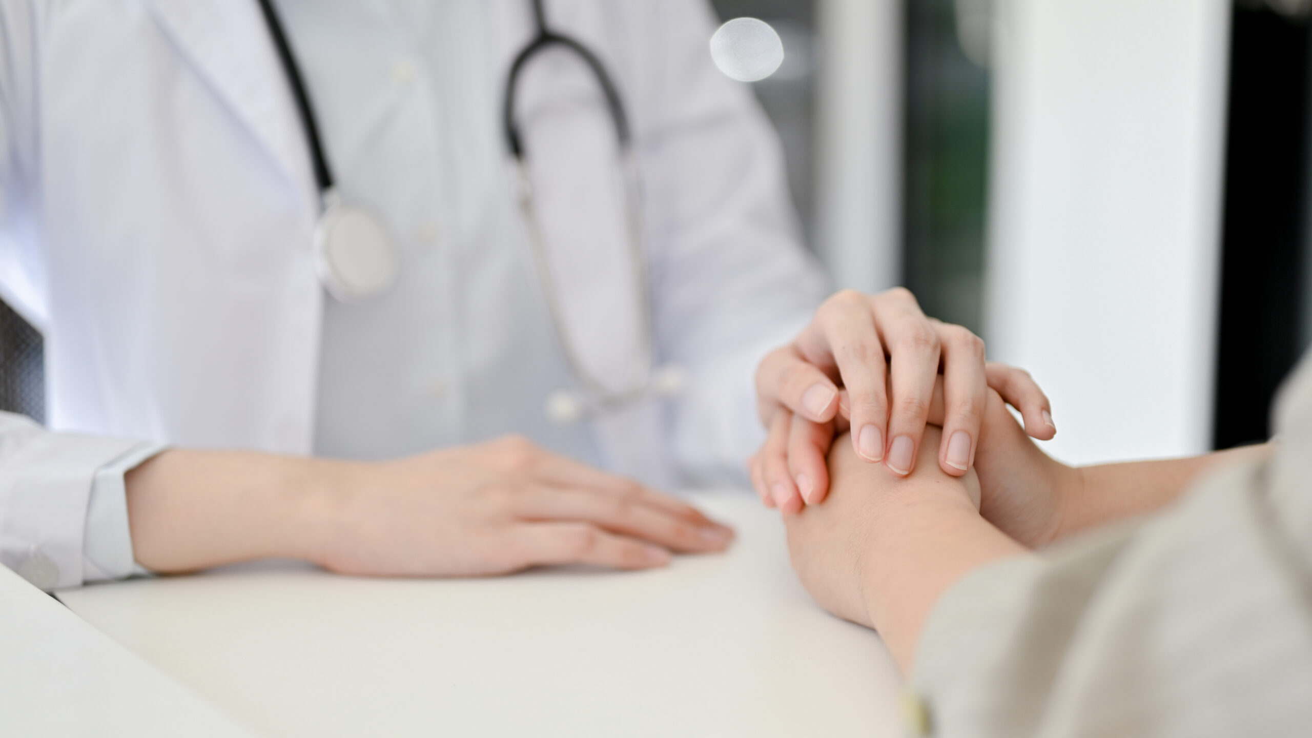Close-up image of a caring female doctor holding a patient’s hands to comfort her during the meeting