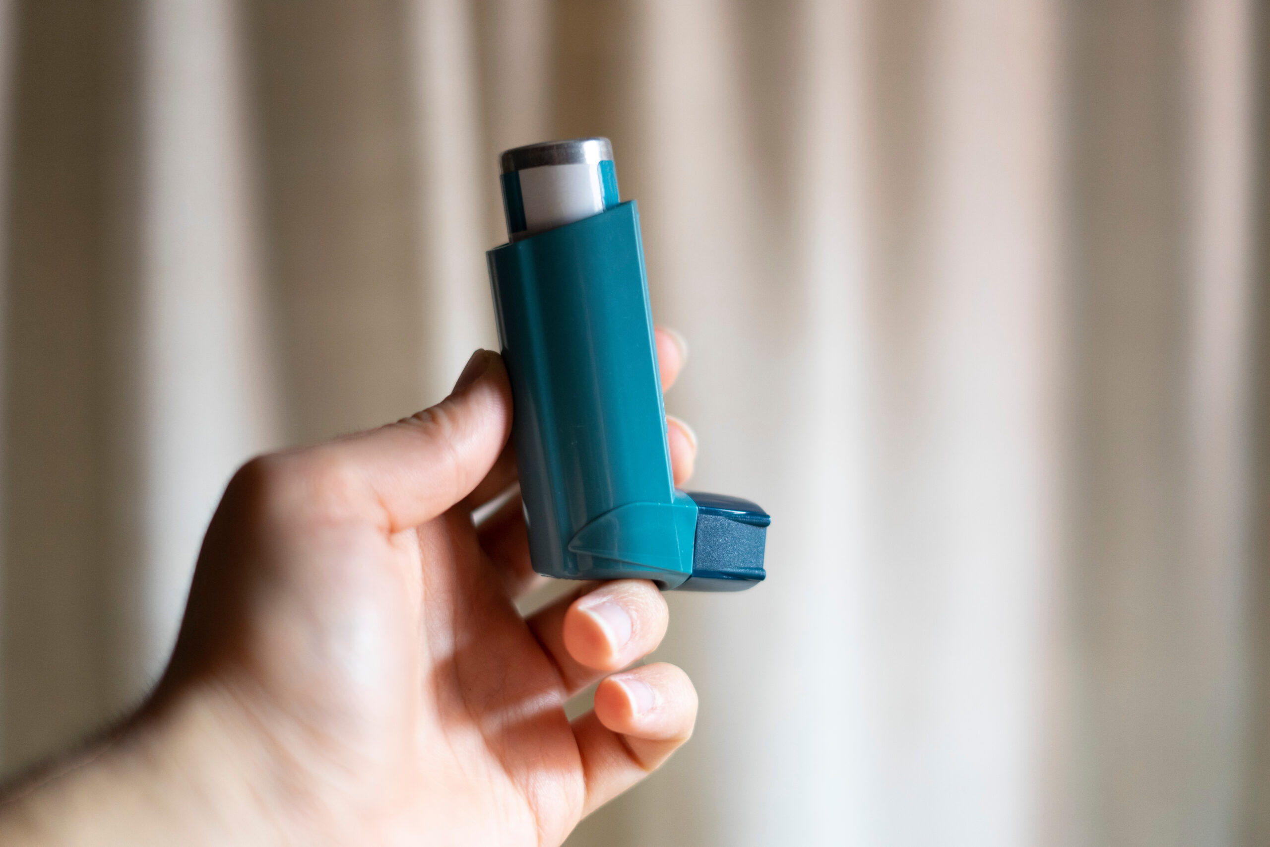 Hand picking up a blue asthma inhaler.